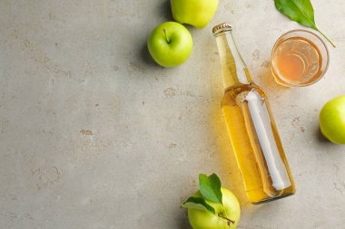 Şişede nefis elma şarabı, gri desenli masada yeşil yapraklı cam ve elmalar, düz yatak. Metin için boşluk