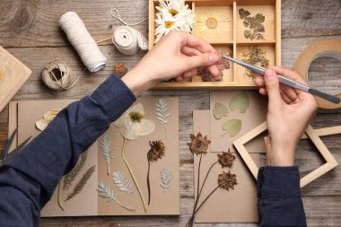 Ahşap masa, üst manzara, kuru çiçekleri deftere koyan kadın.