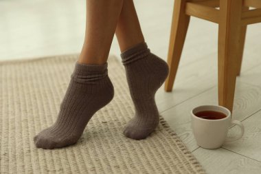 Yumuşak bej halıda çoraplı bir kadın ve evinde bir fincan, yakın plan.