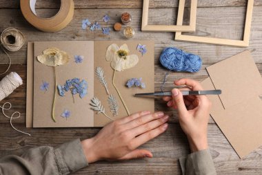 Ahşap masa, üst manzara, kuru çiçekleri deftere koyan kadın.