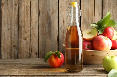 Delicious cider in glass bottle and apples on wooden table. Space for text