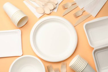Set of disposable tableware on pale orange background, flat lay