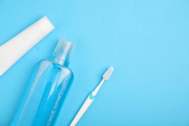 Mouthwash, toothbrush and toothpaste on light blue background, flat lay. Space for text