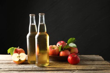 Cam şişelerde nefis elma şarabı ve ahşap masada koyu gri arka planda elmalar. Metin için boşluk