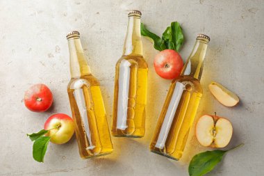 Cam şişelerde nefis elma şarabı ve gri desenli masada elmalar.