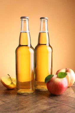 Cam şişelerde lezzetli elma şarabı ve ahşap masada portakal eğimli arka planda elmalar.