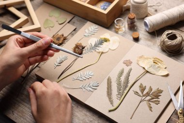 Ahşap masadaki kuru çiçekleri deftere koyan kadın, yakın plan.