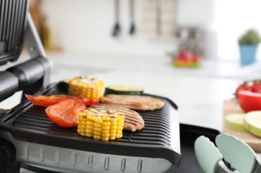 Electric grill with tasty meat and vegetables on table in kitchen, closeup
