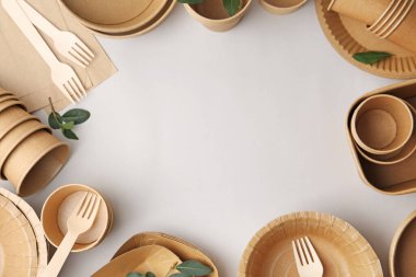 Set of disposable tableware and green leaves on white background, flat lay. Space for text