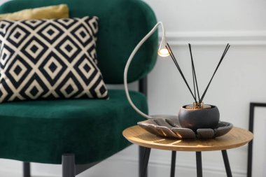 Stylish lamp and reed diffuser on side table near armchair with pillows indoors