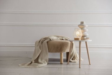 Stylish lamp and vase on white table near pouf indoors