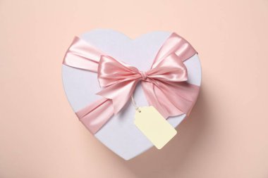 Soluk pembe arka planda boş etiketli kalp şeklinde bir hediye kutusu.