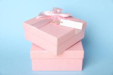 Gift boxes with blank tag on light blue background, closeup