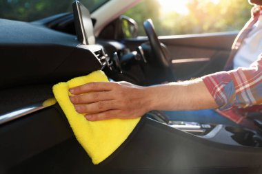Arabadaki paneli sarı mikrofiber bezle silen adam, yakın plan.