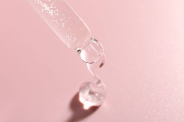 Pembe arka plandaki pipetten kozmetik ürünler damlıyor, yakın plan.