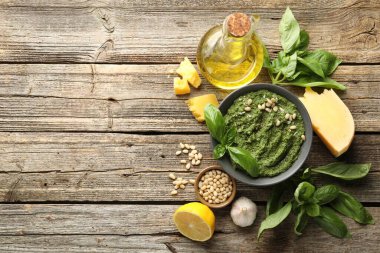 Fresh pesto sauce in bowl and ingredients on wooden table, flat lay. Space for text