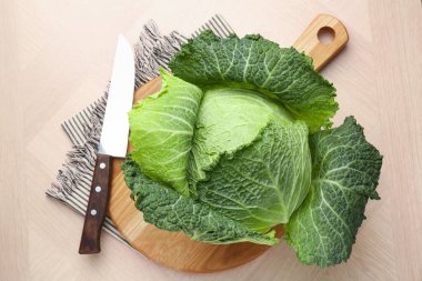 Fresh Savoy cabbage and knife on wooden table, top view