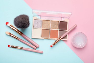 Flat lay composition with colorful eyeshadow palette and makeup brushes on color background