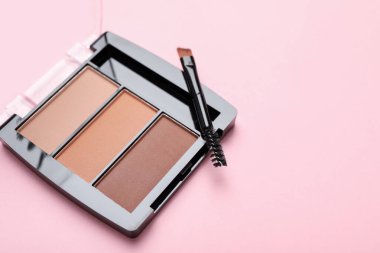 Colorful eyeshadow palette and makeup brush on pink background, closeup. Space for text