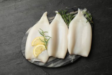 Uncooked squids with lemon slices and rosemary on black table, top view