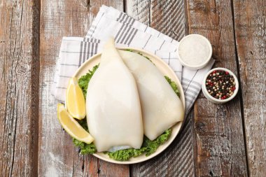 Limon dilimli pişmemiş mürekkep balıkları, ahşap masada marul ve baharatlar.