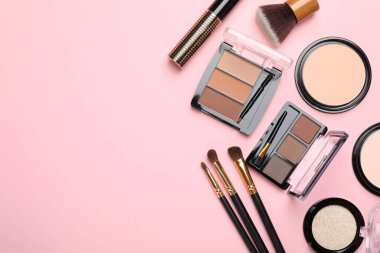 Renkli göz falı paletleri, pudraları ve pembe arka planda makyaj fırçaları olan düz bir kompozisyon. Metin için boşluk