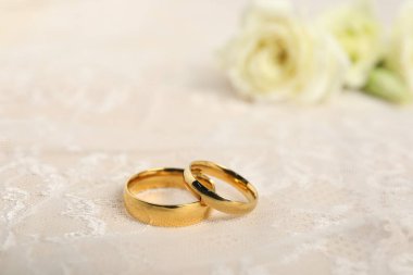 Wedding rings and lace fabric on beige background, closeup