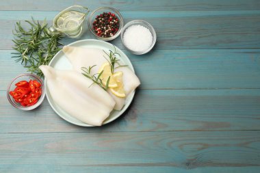 Limon dilimli pişmemiş mürekkep balıkları, biberiye ve baharatlar mavi ahşap masada, düz yerde. Metin için boşluk