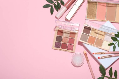 Pembe arka planda göz farı paletleri ve diğer kozmetik ürünleri olan düz bir kompozisyon. Metin için boşluk