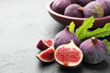 Fresh ripe figs and green leaf on dark textured table, closeup. Space for text