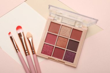 Renkli göz falı paleti ve renk arkaplanı üzerine makyaj fırçaları, düz yatış