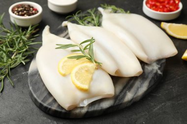 Limon dilimli pişmemiş mürekkep balıkları, biberiye ve baharatlar siyah masada, yakın plan.