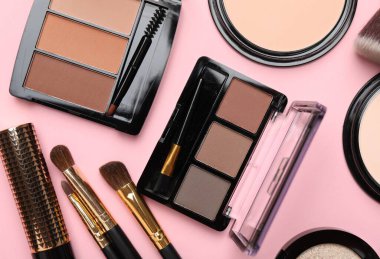 Flat lay composition with colorful eyeshadow palettes, powders and makeup brushes on pink background