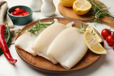 Pieces of raw squids with products on white table, closeup
