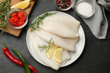 Limon dilimli pişmemiş mürekkep balıkları, biberiye ve baharatlar siyah masada, düz yerde.