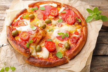 Taking piece of delicious pizza with cheese, tomatoes and olives at wooden table, closeup