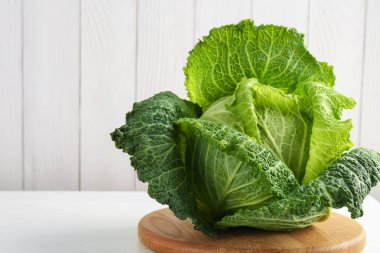 One fresh Savoy cabbage on white wooden table, closeup. Space for text