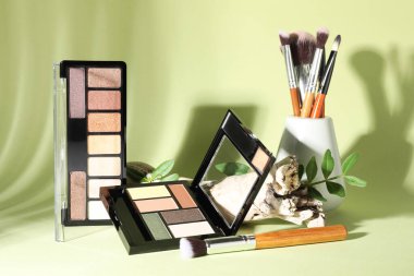 Göz farı paletleri, fırçalar ve soluk yeşil arka planda yapraklar