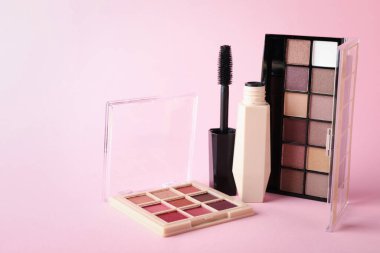 Colorful eyeshadow palettes and mascara on pink background, closeup. Space for text