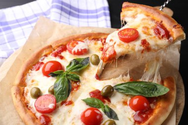 Peynirli, domatesli ve zeytinli lezzetli pizzayı siyah masada yakın plan çekiyoruz.