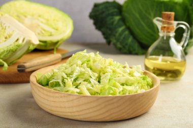 Shredded Savoy cabbage in bowl, knife and oil on light table, closeup