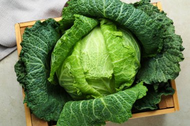 Fresh Savoy cabbage in wooden crate on light grey table, top view