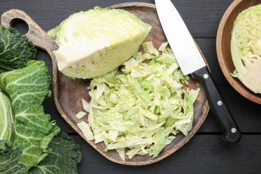 Cut fresh Savoy cabbages and knife on black wooden table, flat lay