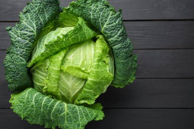 Fresh Savoy cabbage on black wooden table, top view. Space for text