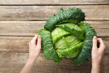 Ahşap masada taze Savoy lahanası tutan kadın, yakın plan.
