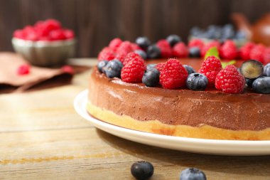 Delicious chocolate cheesecake with berries and mint on wooden table, closeup. Space for text