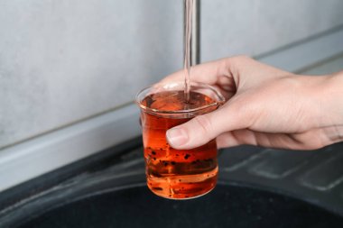 Kadın, kapalı alandaki musluktan su örneği alıyor, yakın plan. Kalite testi