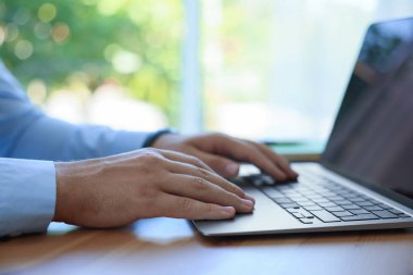 İçerideki ahşap masada dizüstü bilgisayarda çalışan adam, yakın plan.