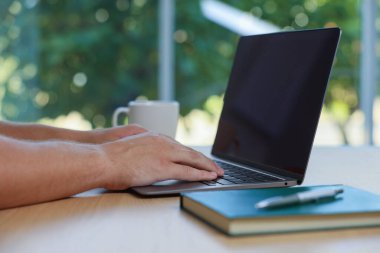 İçerideki ahşap masada dizüstü bilgisayarda çalışan adam, yakın plan.