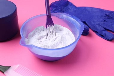 Care cosmetic product for blonde hair in bowl and hairdresser's tools on pink background, closeup